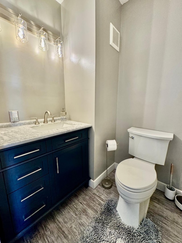 bathroom with toilet, vanity, wood finished floors, and baseboards