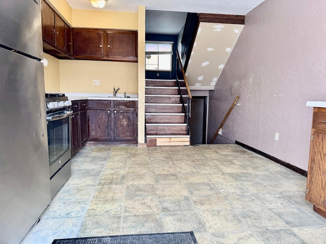 kitchen with appliances with stainless steel finishes, a textured wall, a sink, baseboards, and light countertops