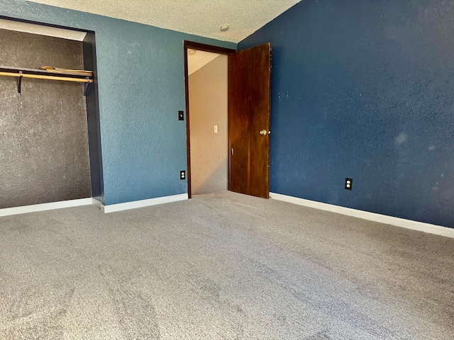 unfurnished bedroom with a textured wall, carpet flooring, a textured ceiling, a closet, and baseboards