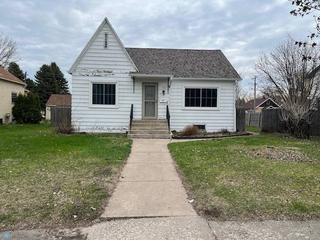 bungalow-style home with roof with shingles, fence, and a front yard