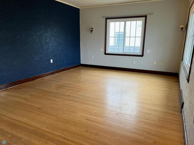 empty room featuring baseboards, a textured wall, ornamental molding, and wood finished floors