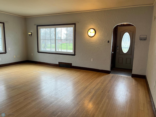 foyer with arched walkways, a textured wall, visible vents, and wood finished floors