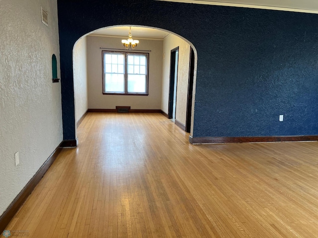 empty room with arched walkways, a textured wall, visible vents, and ornamental molding