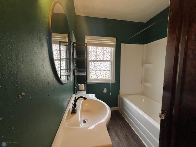 bathroom featuring baseboards, a sink, wood finished floors, and tub / shower combination