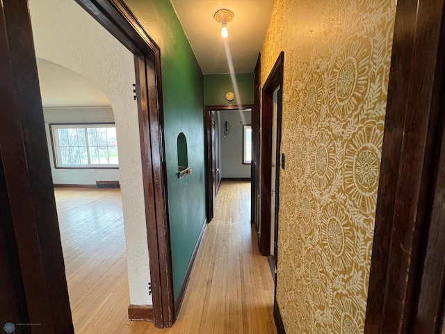 hall with baseboards, arched walkways, a textured wall, and wood finished floors