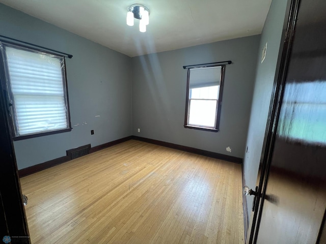 empty room with baseboards, visible vents, and light wood finished floors