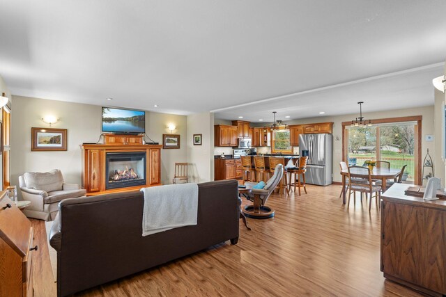 living area with light wood-style floors, an inviting chandelier, a glass covered fireplace, and recessed lighting