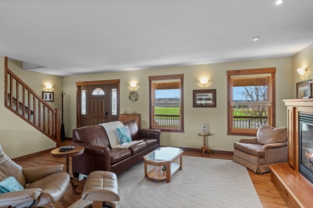 living area with plenty of natural light, stairs, a glass covered fireplace, and baseboards