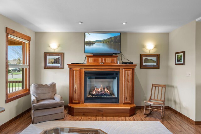 living area with recessed lighting, baseboards, a glass covered fireplace, and wood finished floors