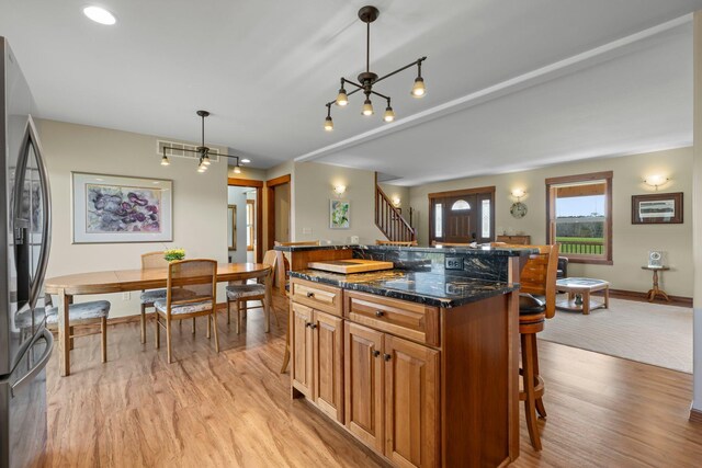 kitchen featuring brown cabinets, light wood-style flooring, a center island, a kitchen bar, and stainless steel refrigerator with ice dispenser