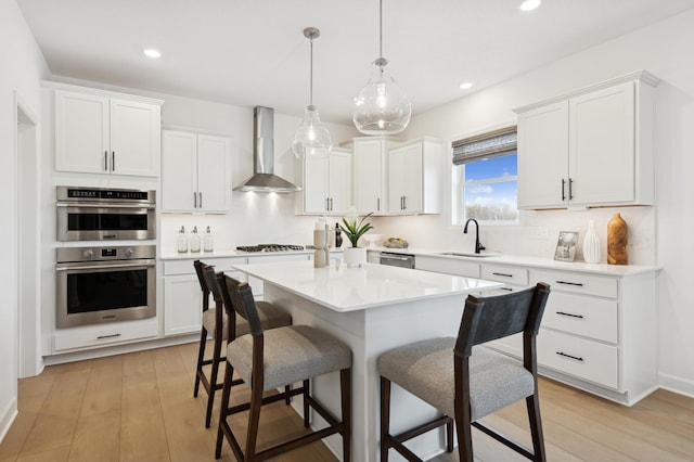 kitchen with wall chimney range hood, a kitchen breakfast bar, a sink, stainless steel appliances, and white cabinets