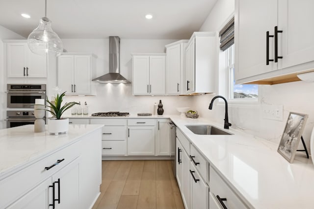 kitchen featuring wall chimney exhaust hood, stainless steel appliances, a sink, recessed lighting, and white cabinetry