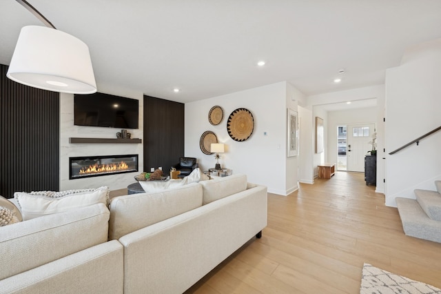 living area featuring light wood-type flooring, baseboards, a glass covered fireplace, recessed lighting, and stairs
