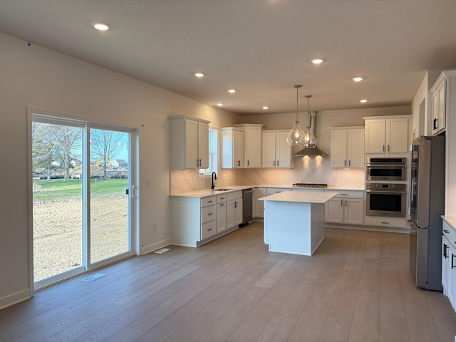 kitchen featuring wall chimney range hood, a center island, a sink, stainless steel appliances, and light countertops