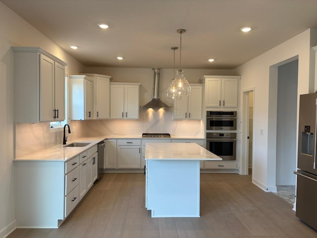 kitchen with a center island, a sink, wall chimney exhaust hood, appliances with stainless steel finishes, and recessed lighting