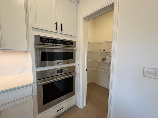 kitchen with light stone countertops, tile patterned flooring, white cabinetry, and double oven