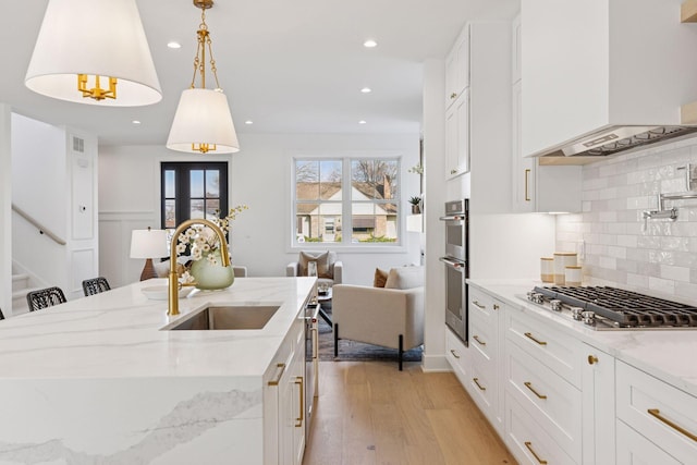 kitchen with premium range hood, stainless steel appliances, a sink, light wood finished floors, and backsplash