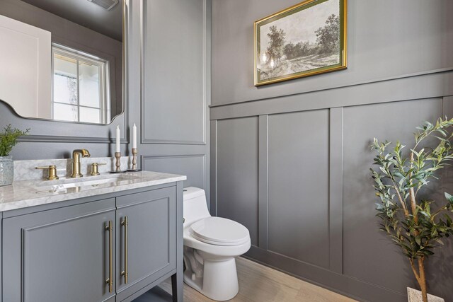 bathroom featuring a decorative wall, toilet, and vanity