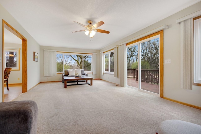 living room with a ceiling fan, baseboards, and light colored carpet