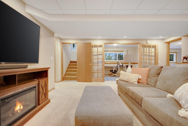 carpeted living area with a drop ceiling, stairway, and a glass covered fireplace