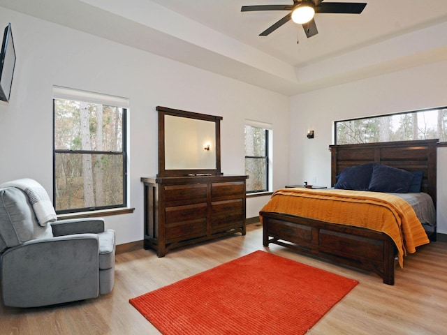 bedroom featuring ceiling fan, light wood-type flooring, a tray ceiling, and multiple windows