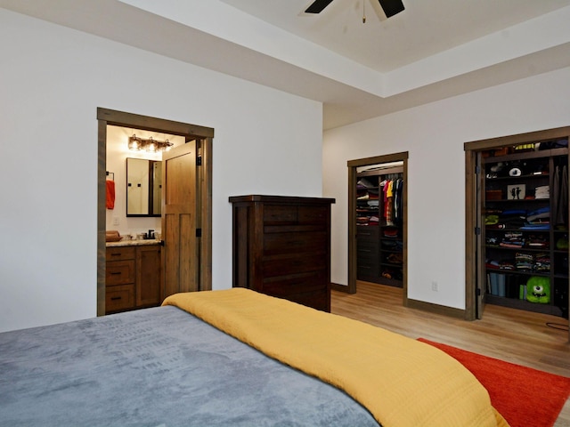 bedroom featuring baseboards, light wood-type flooring, ensuite bath, and a spacious closet