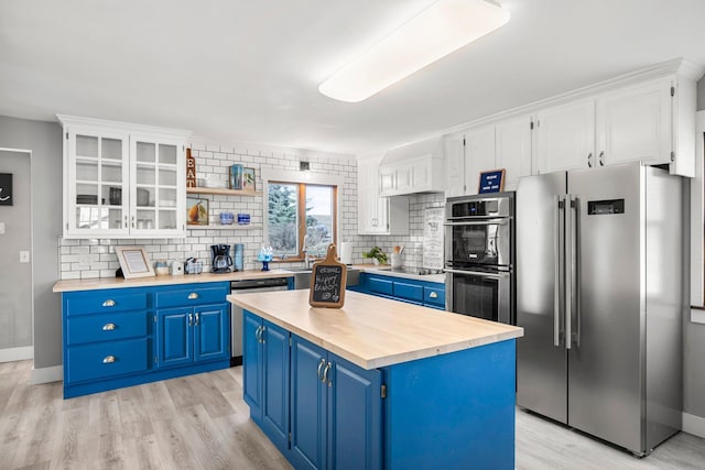 kitchen with light wood finished floors, wood counters, blue cabinetry, backsplash, and appliances with stainless steel finishes