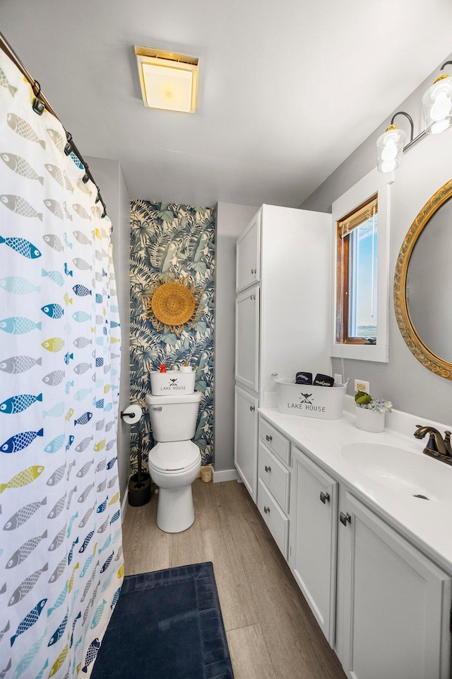 bathroom with vanity, toilet, baseboards, wallpapered walls, and wood finished floors