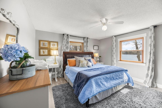 bedroom featuring baseboards, ceiling fan, a textured ceiling, and light wood-style flooring