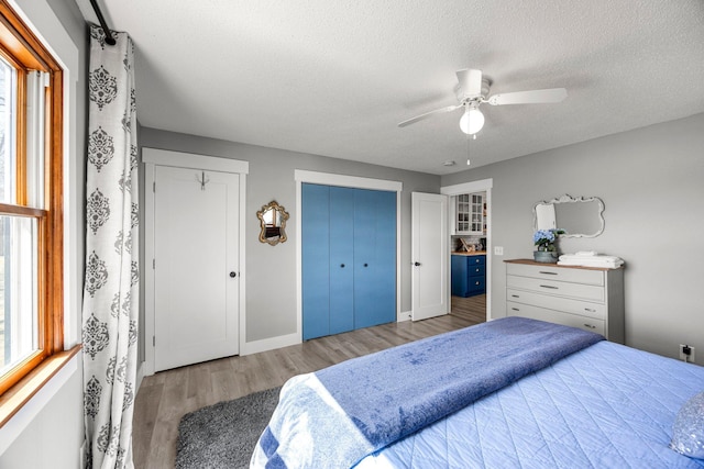 bedroom with a textured ceiling, two closets, baseboards, wood finished floors, and a ceiling fan