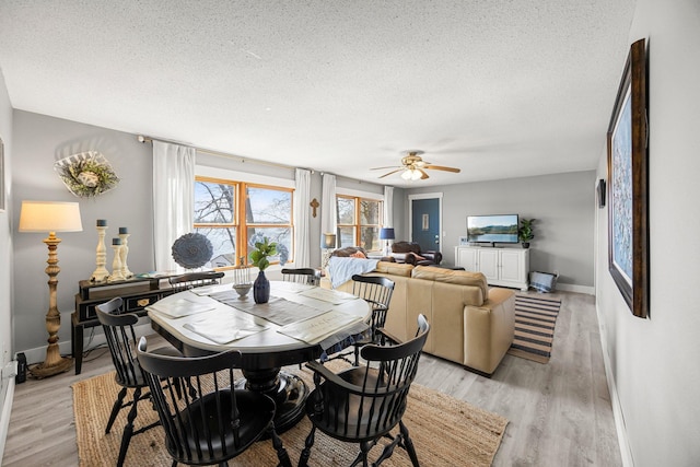 dining space featuring light wood finished floors, a textured ceiling, ceiling fan, and baseboards