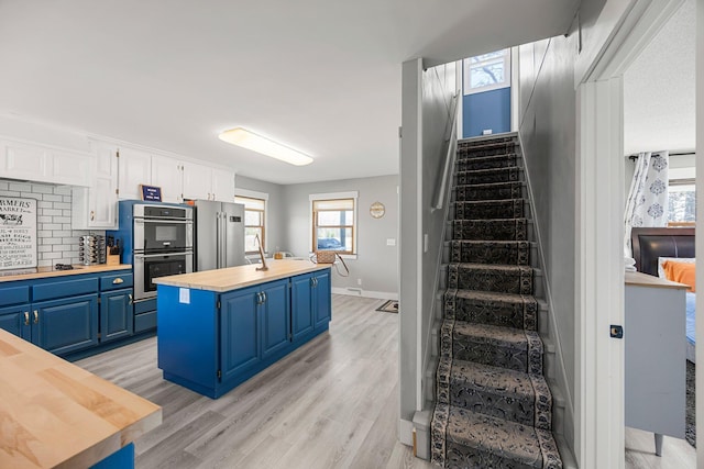 kitchen with wood counters, light wood-style floors, stainless steel appliances, blue cabinets, and a kitchen island
