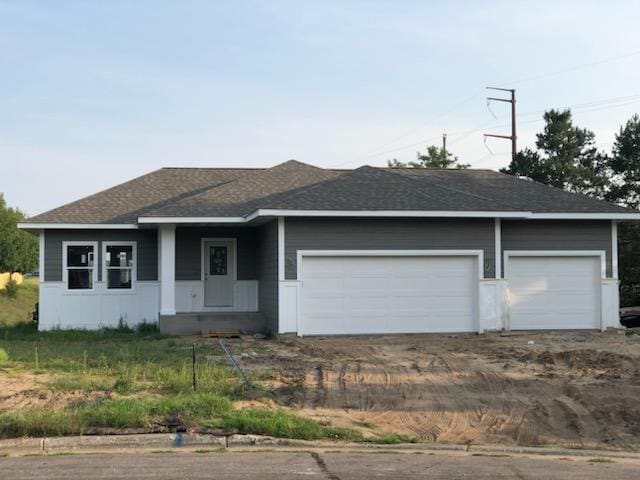 ranch-style home featuring dirt driveway, a shingled roof, and a garage