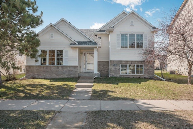 split level home featuring brick siding, roof with shingles, and a front yard