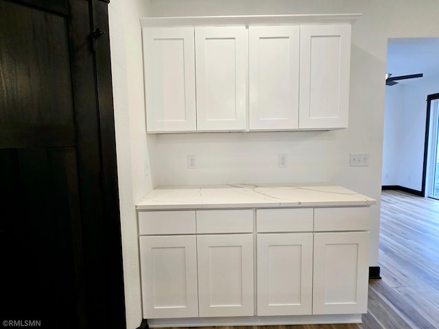 kitchen with white cabinets, light stone counters, and wood finished floors