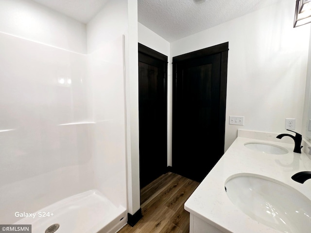 bathroom with wood finished floors, a sink, a shower stall, and double vanity