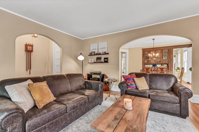 living area featuring crown molding, light wood-style floors, arched walkways, a chandelier, and baseboards