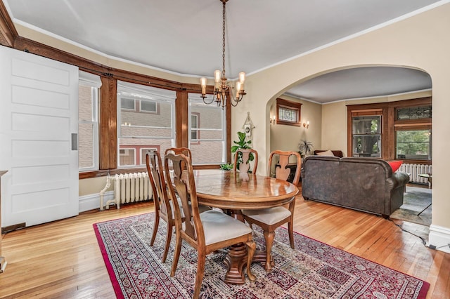 dining area with a notable chandelier, arched walkways, light wood-style flooring, radiator, and ornamental molding