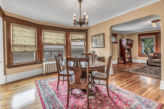 dining room featuring arched walkways, a chandelier, radiator, wood finished floors, and ornamental molding