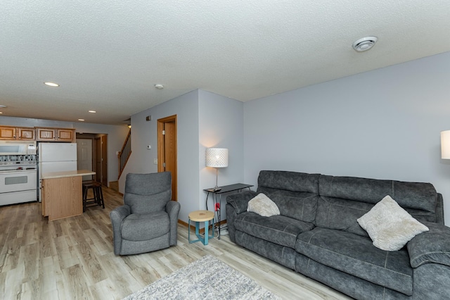 living room featuring a textured ceiling, light wood-type flooring, recessed lighting, and stairs