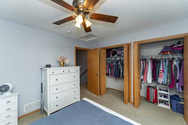 carpeted bedroom with ceiling fan, two closets, visible vents, baseboards, and a textured ceiling