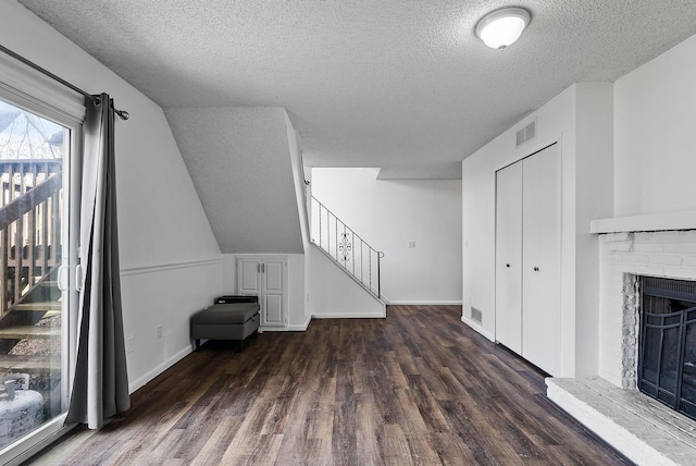 unfurnished living room with a textured ceiling, wood finished floors, stairs, a fireplace, and baseboards