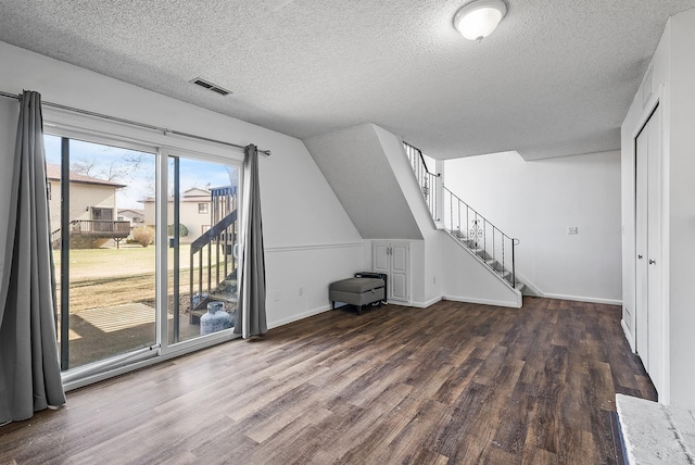 unfurnished living room featuring wood finished floors, a textured ceiling, stairway, baseboards, and vaulted ceiling