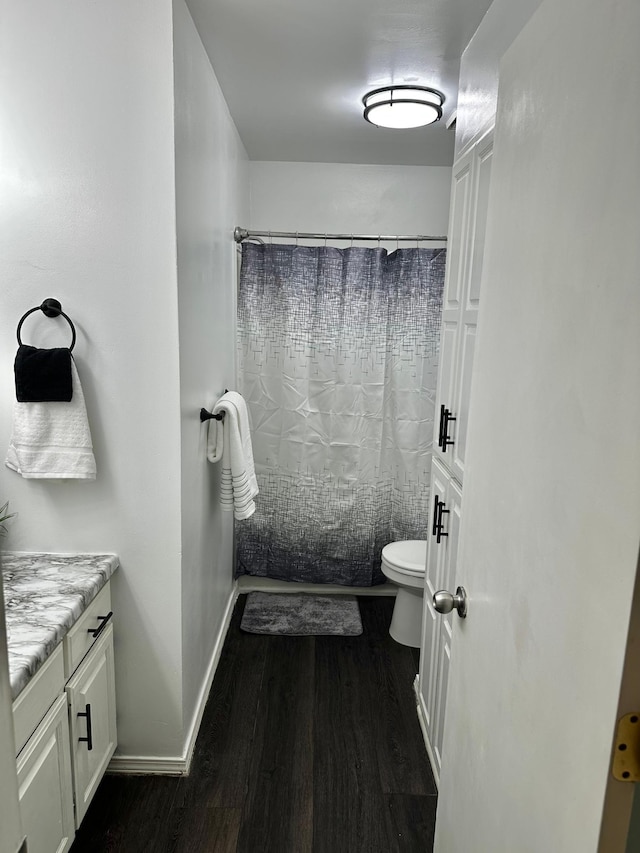 bathroom with toilet, wood finished floors, vanity, baseboards, and shower / bath combo with shower curtain