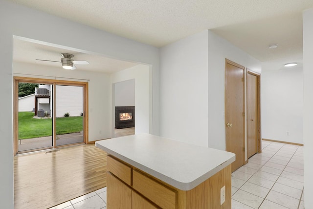 8722 Norway St NW, Coon Rapids, MN 55433 - kitchen featuring light tile patterned floors, a kitchen island, light countertops, a multi sided fireplace, and ceiling fan