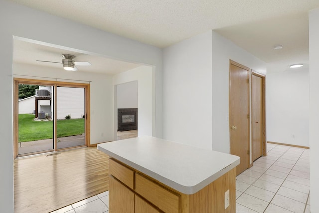 8722 Norway St NW, Coon Rapids, MN 55433 - kitchen with light tile patterned flooring, a kitchen island, light countertops, a glass covered fireplace, and ceiling fan