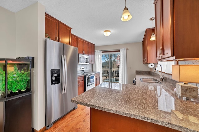 kitchen with a textured ceiling, a sink, appliances with stainless steel finishes, and light wood-style floors