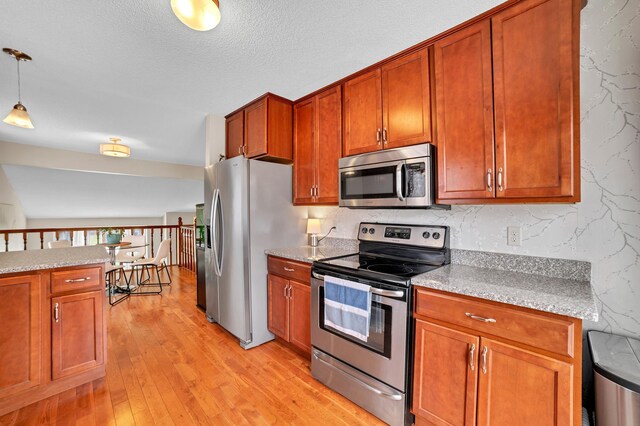 kitchen featuring a textured ceiling, light wood-style flooring, stainless steel appliances, decorative light fixtures, and brown cabinetry