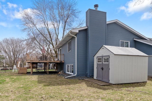 back of house with a chimney, an outbuilding, a storage shed, a wooden deck, and a lawn