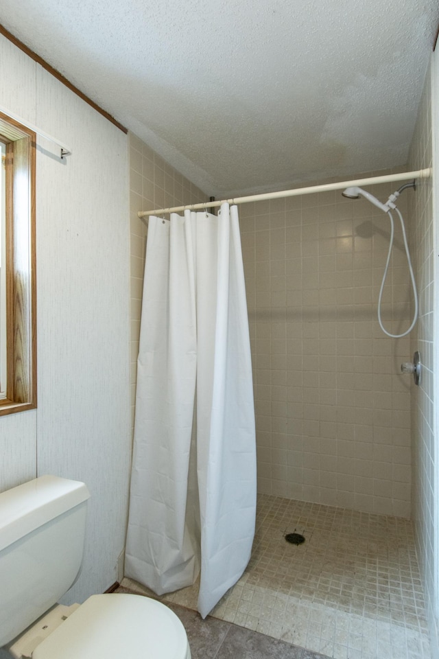 full bath with toilet, a textured ceiling, and tiled shower